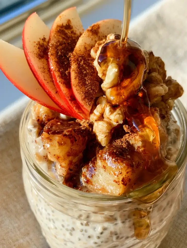 A handheld smartphone photo showing the top view of the apple cinnamon overnight oats with a glossy maple syrup drizzle and cinnamon dusting.