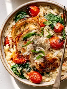 Top-down view of a creamy orzo dish with sliced seared chicken and fresh basil. (Simple and tasty recipe)