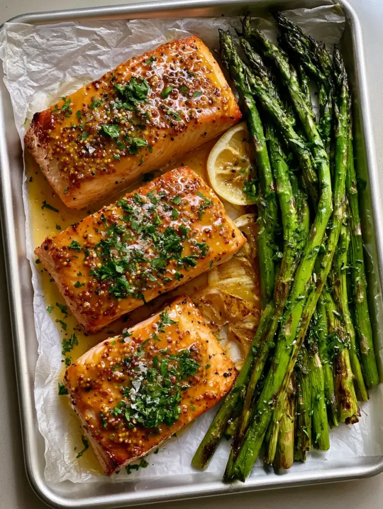 Close up of charred asparagus and caramelized lemon rounds on a sheet pan. (Honey Dijon Baked Salmon)