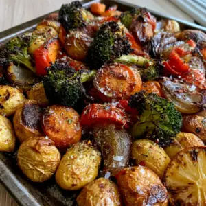 Close up photo of golden-brown roasted baby potatoes and charred broccoli tips in a metal pan. (One-Pan Roasted Vegetables)