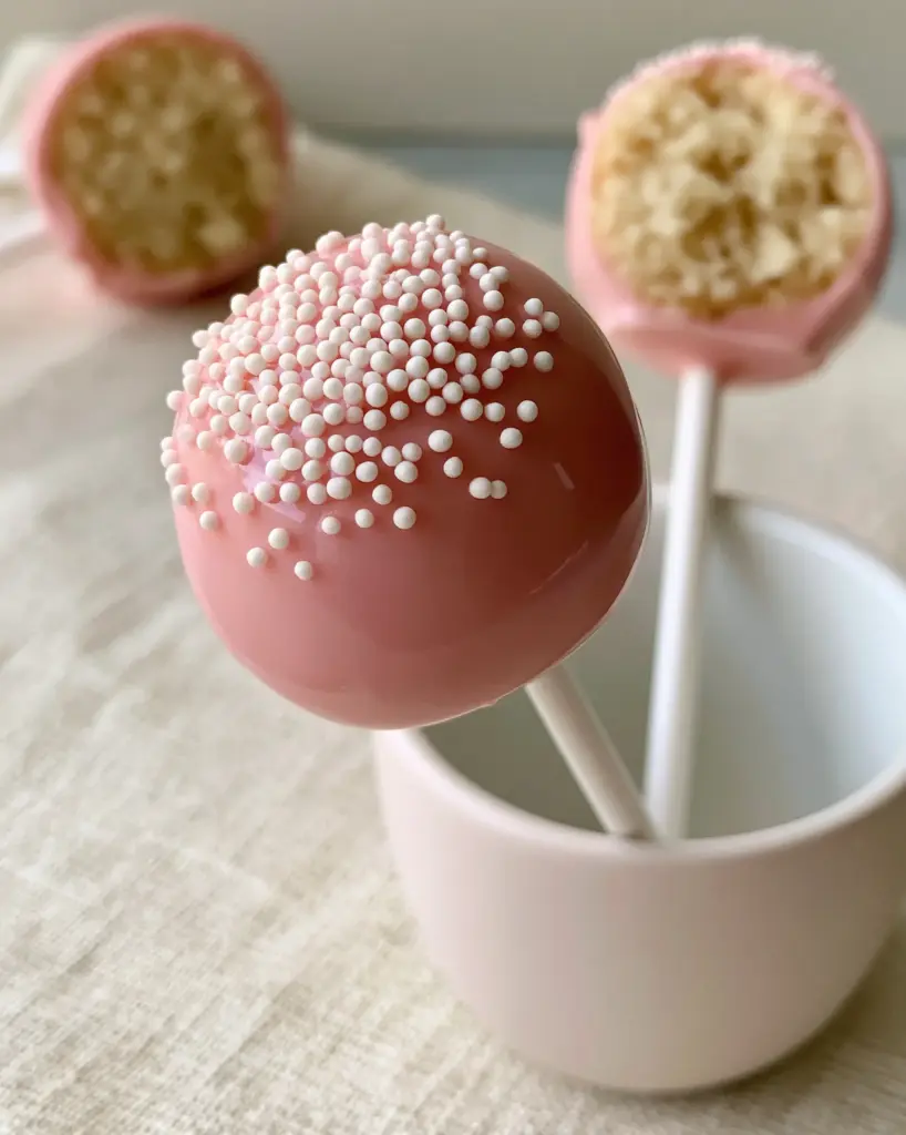 Cake Pop Recipes: The Ultimate Starbucks Copycat Guide 1 A halved cake pop showing the moist, dense vanilla cake crumb interior next to whole pink cake pops.
