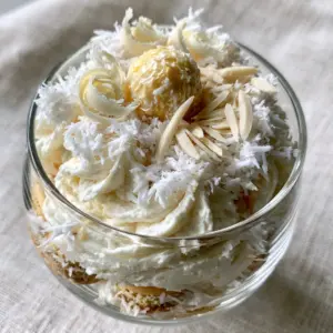 Close up of Raffaello Tiramisu in a glass cup with white chocolate curls and shredded coconut highlights.