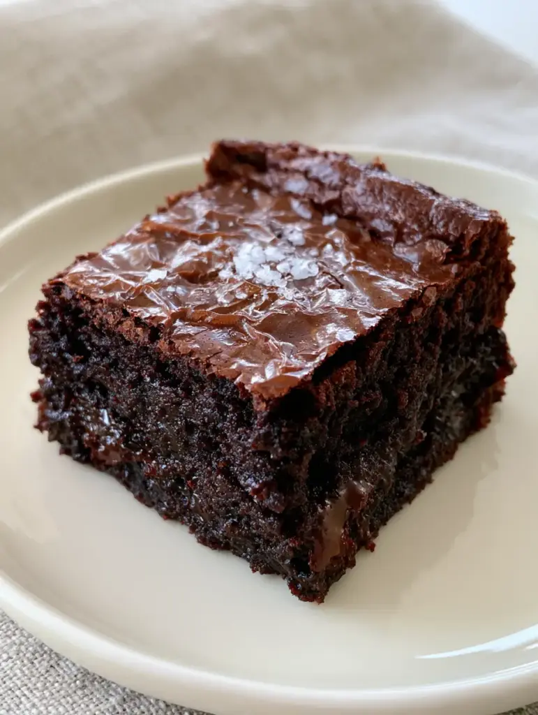 brownie recipe for Ultra-Fudgy Dark Chocolate Brownies 1 A close-up smartphone photo of dense, dark chocolate-brown brownies showing moist interiors with melted chocolate pockets and a light sprinkle of flaky sea salt.